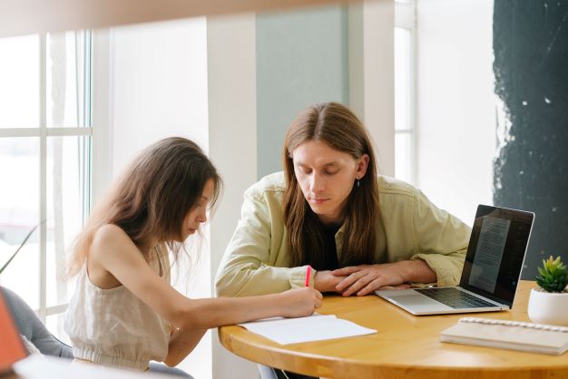 Far og datter laver lektier ved spisebord i deres hjem